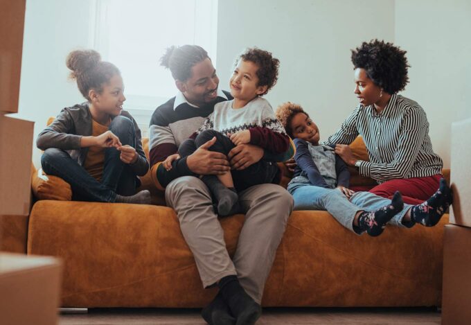 Family sits together on couch after moving into new home purchased a Fannie Mae loan program.