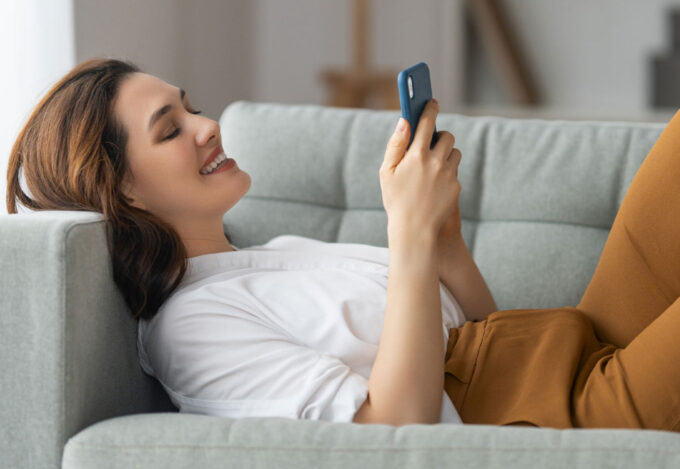 Woman laying on couch enters a mortgage pre-approval into her cell phone.
