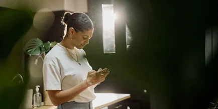 Woman in a white t-shirt looking at her phone in a warmly lit bathroom